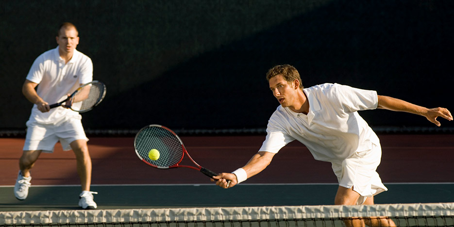 Men playing tennis while wearing appropriate tennis apparel